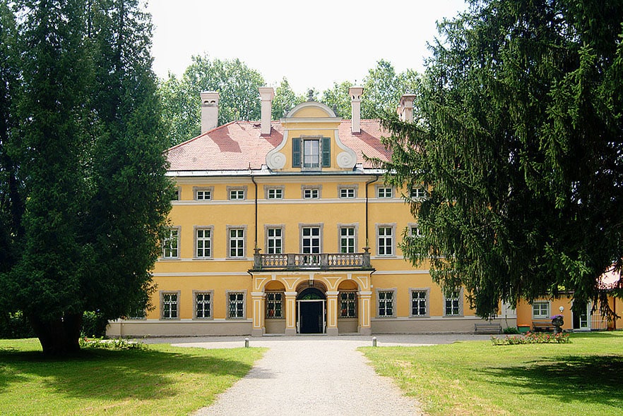 The yellow Baroque façade of Schloss Frohnburg on Hellbrunner Allee, Salzburg; the famous filming location for the front exterior of the Von Trapp villa in The Sound of Music, framed by tall trees.