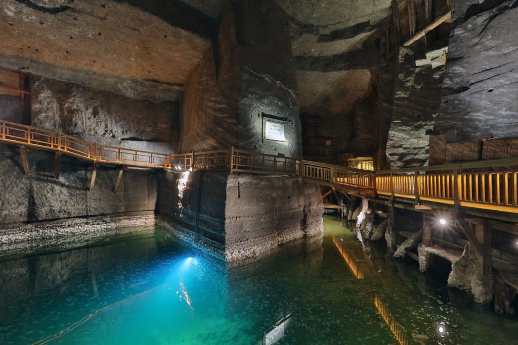 Wieliczka Salt Mine: A Journey into Poland's Underground Wonder - 
Interior view of the Wieliczka Salt Mine featuring a historic wooden winch mechanism and drainage system surrounded by rough, salt-encrusted cavern walls under dim warm lighting.