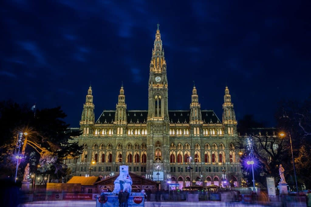 The illuminated Neo-Gothic Vienna City Hall (Rathaus) at night during winter, featuring the Wiener Eistraum ice skating rink and a large Coca-Cola polar bear statue.
