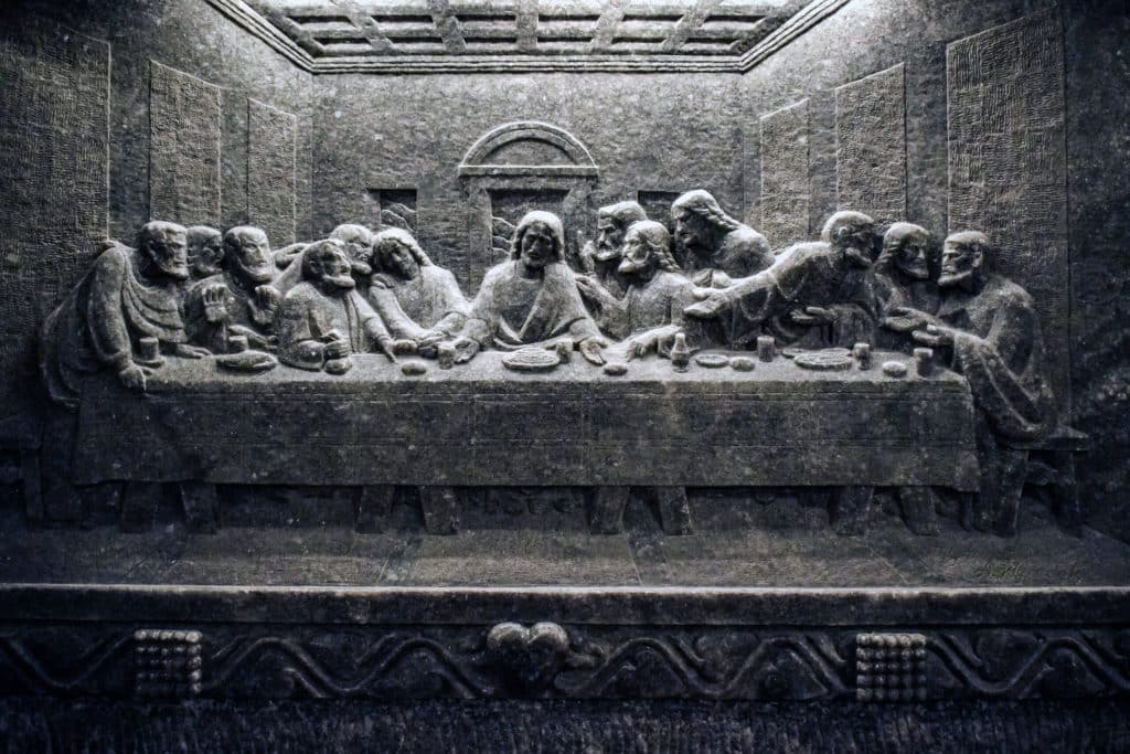 A rock salt bas-relief carving of The Last Supper in the Wieliczka Salt Mine, depicting Jesus and the twelve disciples seated at a long table, sculpted into a grey salt wall.