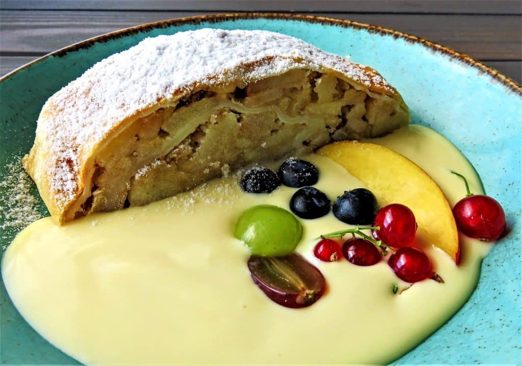 A slice of apple strudel showing thin layers of translucent pastry and a filling of tart apples and raisins.