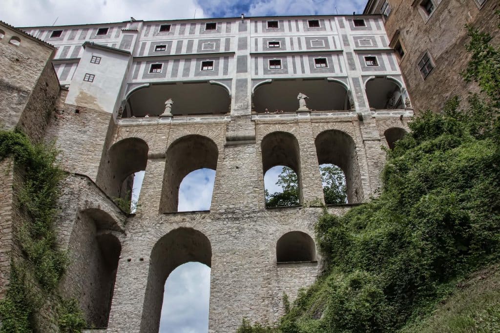 Low angle view looking up at the massive stone arches of the Cloak Bridge (Plášťový most) in Český Krumlov connecting castle buildings.