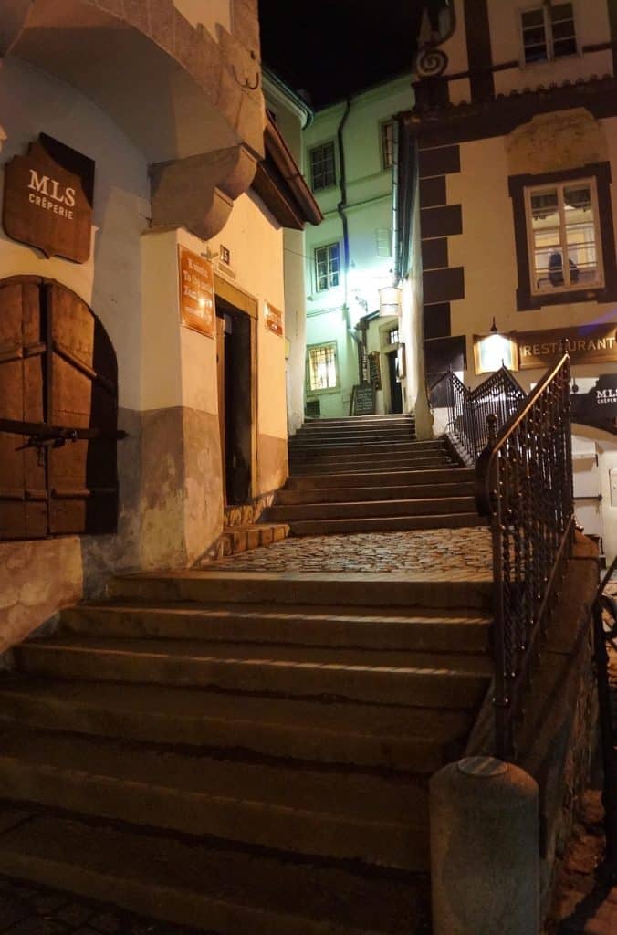 narrow cobblestone street in Český Krumlov at night, illuminated by a single warm street lamp attached to a historic building.