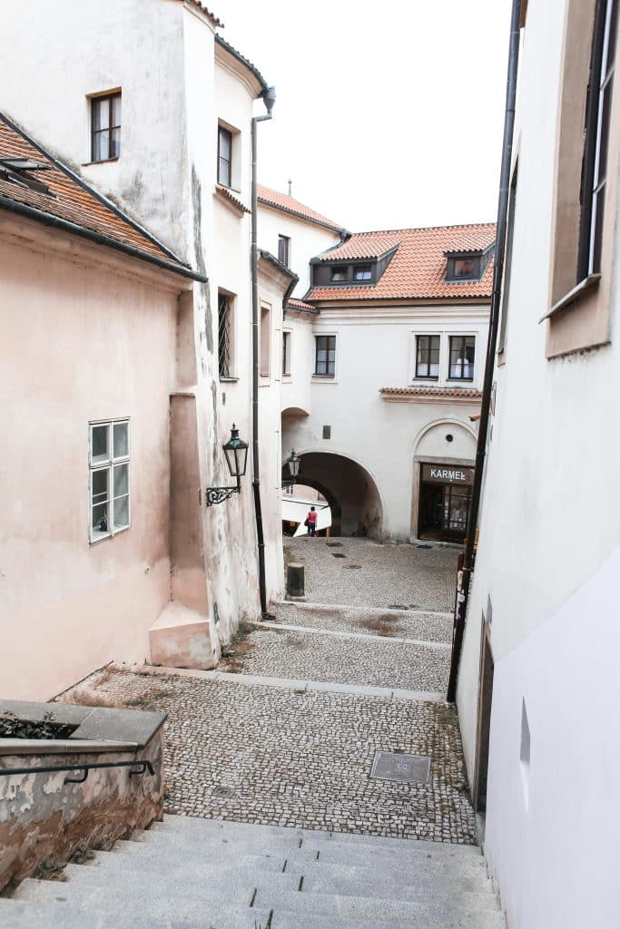 A narrow, downward-sloping cobblestone street with stairs winding between old white buildings, leading through a stone archway; a shop sign reads "KARMEL".