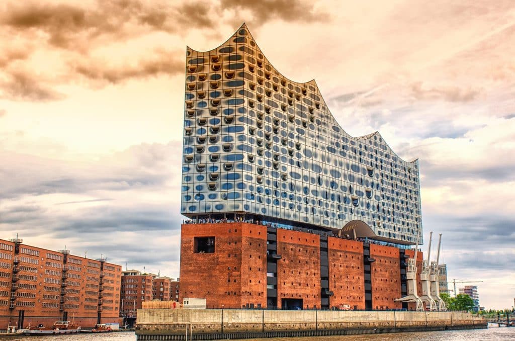 The Elbphilharmonie concert hall in Hamburg, featuring a modern glass wave structure built on top of a historic red brick warehouse at the harbor.