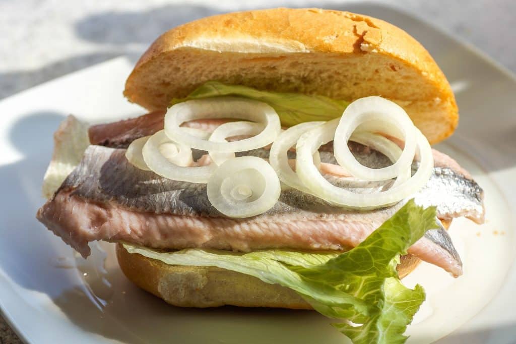 Close-up of a traditional Hamburg Fischbrötchen (fish sandwich) with fresh herring and onions on a crusty roll.