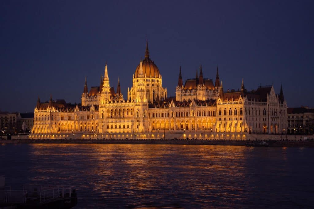 The Hungarian Parliament building illuminated in golden light at night, reflecting brightly in the Danube River.