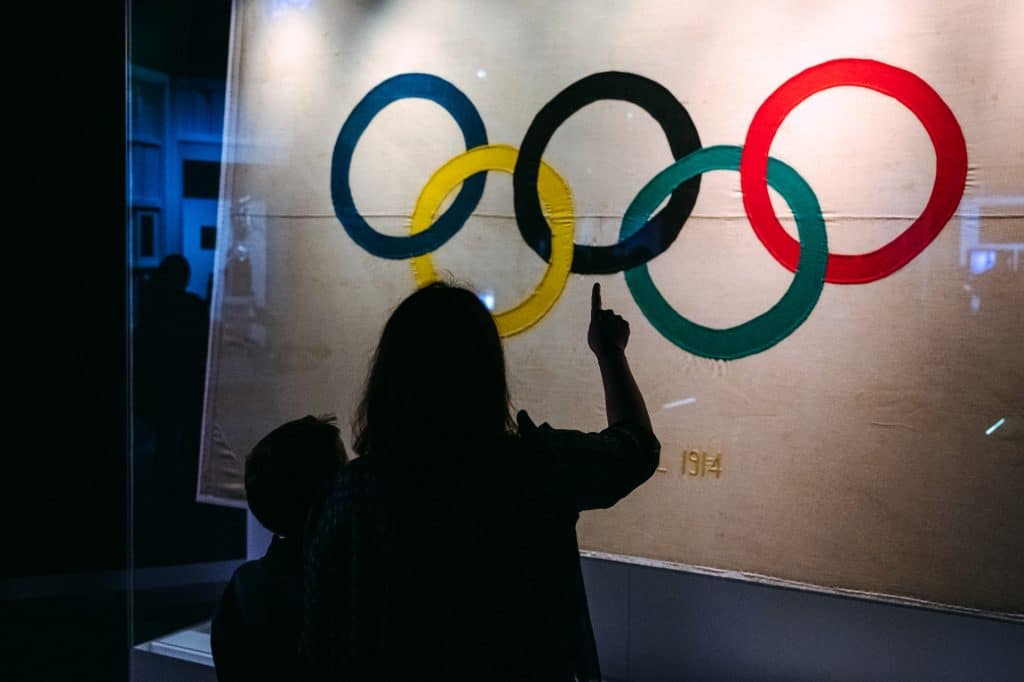 Silhouette of a woman and child pointing at the Olympic Rings inside a darkened interactive exhibit at the Olympic Museum.