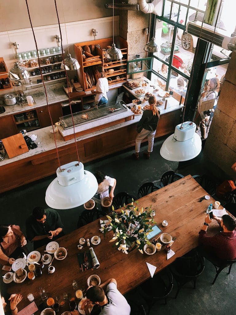 Overhead flat-lay photograph of a cup of coffee, a notebook, and a croissant on a wooden café table.