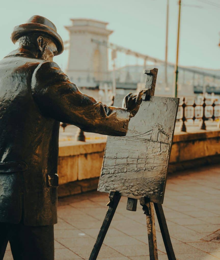 Bronze statue of a painter with an easel sketching the Chain Bridge on the Danube embankment.