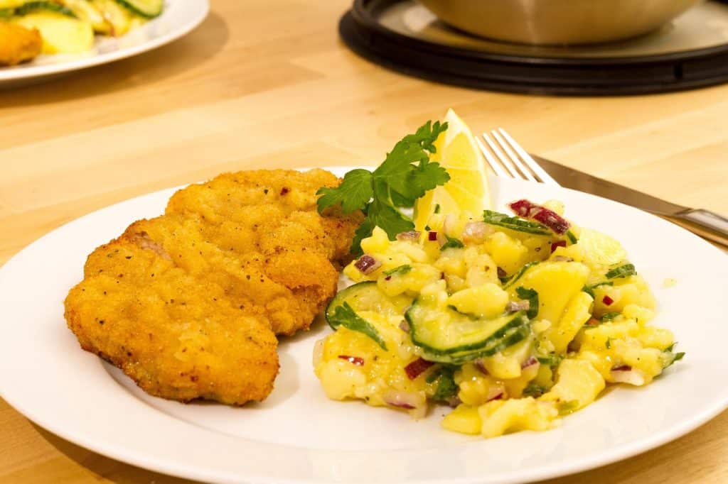 Authentic veal Wiener Schnitzel with a crispy, rippled breadcrumb coating, served with a lemon wedge and traditional Austrian potato salad.