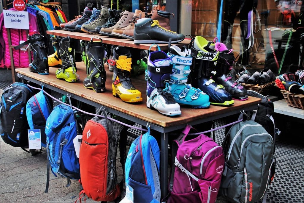 A shop display on a sidewalk featuring colorful hiking backpacks and heavy-duty mountaineering boots on shelves.