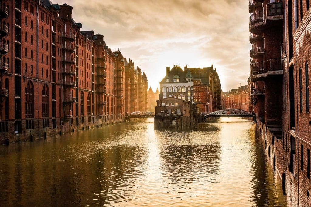 Golden hour sunlight reflecting off the canal waters in Hamburg's UNESCO Speicherstadt warehouse district, highlighting the historic red brick architecture.