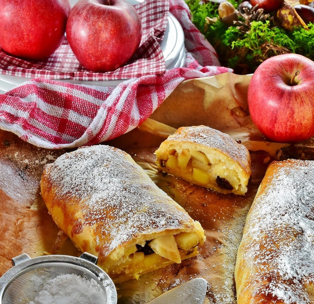 Baked apple strudel rolls dusted with powdered sugar, with one sliced open to show the apple and raisin filling.