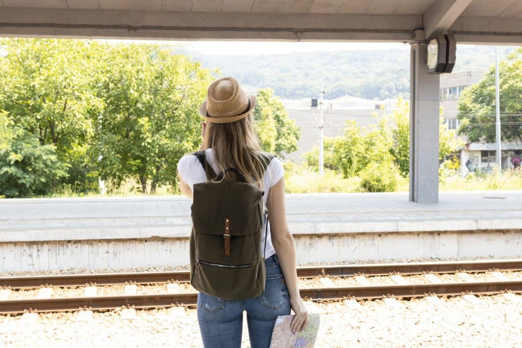 View from behind of a traveler in a hat looking out a train window at passing green hills.