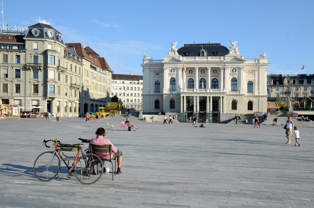 Wide shot of the Zurich Opera House and Sechseläutenplatz, featuring casual seating and a bicycle in the foreground.